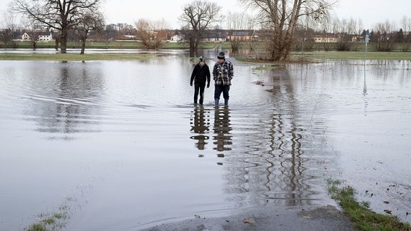 Lothar und sein Enkel Yannick gehen mit Gummistiefeln durch das Hochwasser der Elbe.