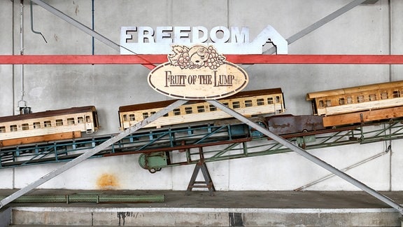 "Freedom" steht an einer Wand, dadrunter "Fruit of the Loop". Es sind drei mittelgroße Eisenbahnwaggons zu sehen.