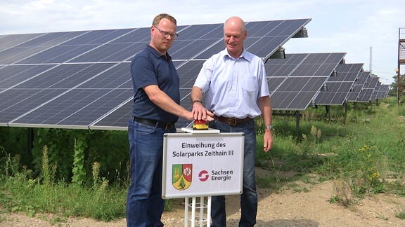 Mirko Pollmer, Bürgermeister von Zeithain und Rutger Kretschmer von SachsenEnergie drücken den roten Knopf an einer Solaranlage in Zeithain
