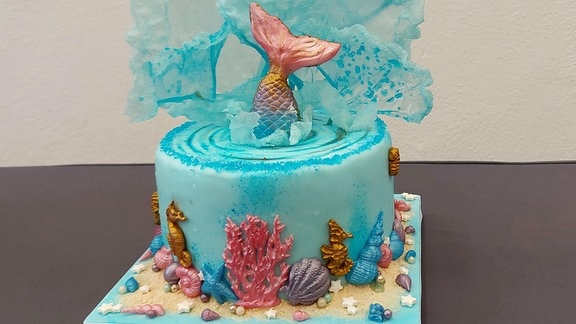 Eine große blaue Torte zeigt eine Unterwasserszenerie mit einem Fisch, der ins Wasser springt und Wasser verspritzt. Nur die Flosse ragt heraus.