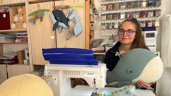 Ein Frau sitzt mit einem Kuscheltier vor einer Nähmaschine. 