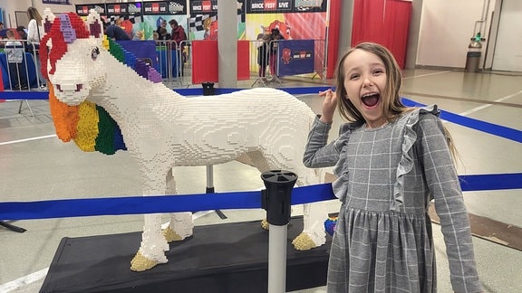 Ein fröhliches Mädchen steht vor einem Einhorn aus Lego