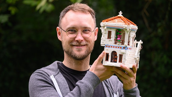 Martin Gebert, Lego-Baumeister aus Dresden, hält ein Haus aus Legosteinen in der Hand.