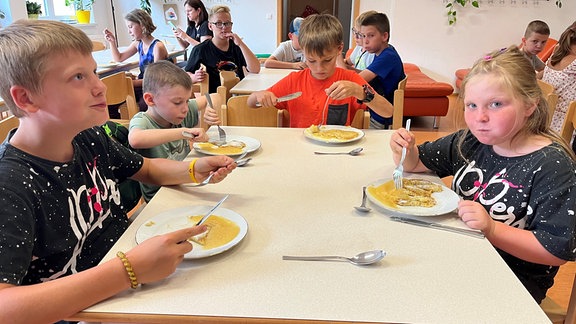 Kinder sitzen am Tisch und essen gemeinsam