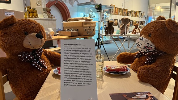 Zwei braune Teddys sitzen an einem Tisch.