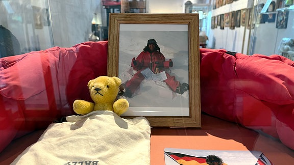 Ein orgefarbener Teddy in einer Vitrine neben einem Bild von einem Mann in einem schneereichen Gebiet