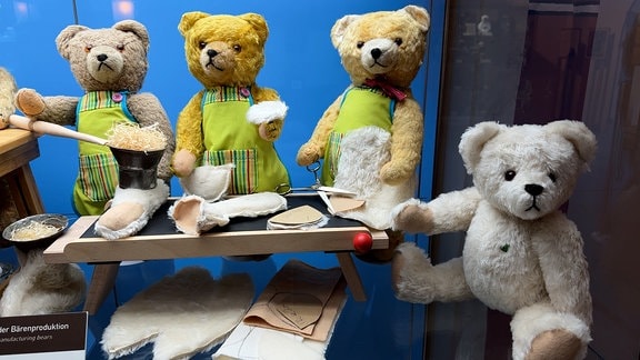Vier Teddys sitzen in einer Vitrine. 
