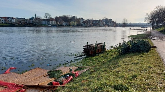 Am überschwemmten Ufer der Elbe liegt ein Weihnachtsbaum, stehen ein paar zusammengeklappte Bierbänke und Pappbündel. Mehr ist vom Weihnachtscircus und der Festweise in Meißen nach Weihnachten 2023 nicht zu sehen. Das Hochwasser hat alles verdrängt.