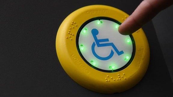 Symbolbild: Ein Zeigefinger drückt auf einen Knopf mit einem Rollstuhlfahrer-Symbol, das grün aufleuchtet