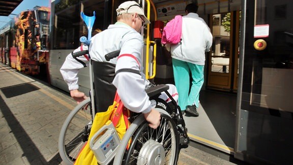 Ein Rollstuhlfahrer fährt über eine Kante in eine Straßenbahn.