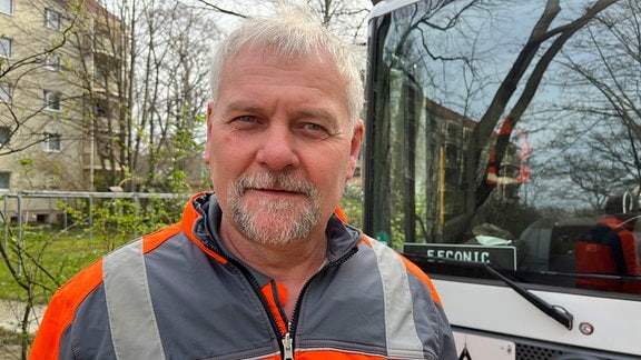 Ein Mann mit orange-beiger Jacke steht vor einem Lkw.