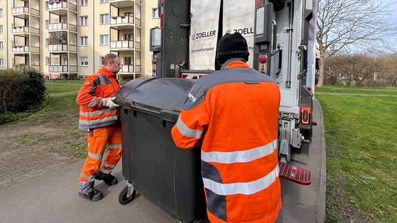 Zwei Müllmanner rollen eine Rolltonne zum Müllauto.