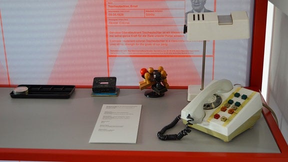 Impressionen einer DDR Ausstellung, ein Telefon, Stempel, ein Locher. Dahinter Informationen auf einer Tafel.