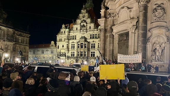 Demonstranten stehen am Schlossplatz in Dresden und halten Schilder gegen Pegida hoch. Polizeiautos trennen die Gegenprotestierer von der Pegida-Demo ab.