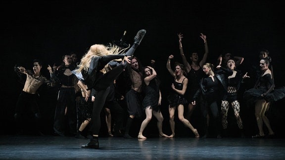 Szene aus dem Tanztheaterstück "Wonderful World": Tänzerinnen und Tänzer in knappen, schwarzen Party-Outfits tanzen auf einer Bühne.