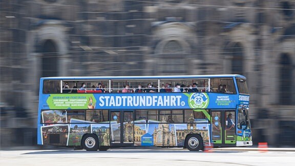 Ein blauer Doppeldecker-Bus der Stadtrundfahrt Dresden GmbH fährt mit Touristen über den Theaterplatz. 