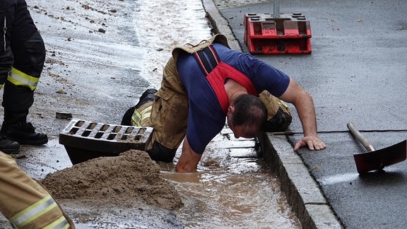 Ein Feuerwehrmann versucht den Durchfluss an einem Gullyschacht zu verbessern