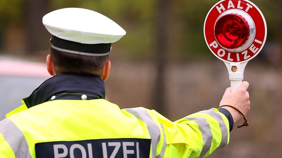 Polizeibeamter der Verkehrspolizei hält bei einer Verkehrskontrolle eine Kelle mit Aufschrift "Halt Polizei" hoch.