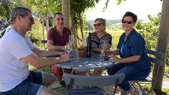 Mehrere Menschen sitzen an einem Tisch und trinken Wein. 