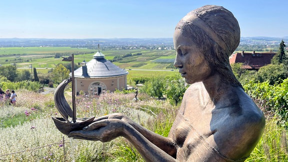 Eine Statue steht auf einem Berg vor einer Weinlandschaft.