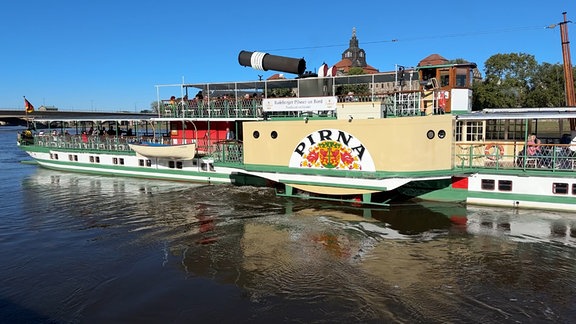 Ein helles Schiff legt an einem Fluss ab. 