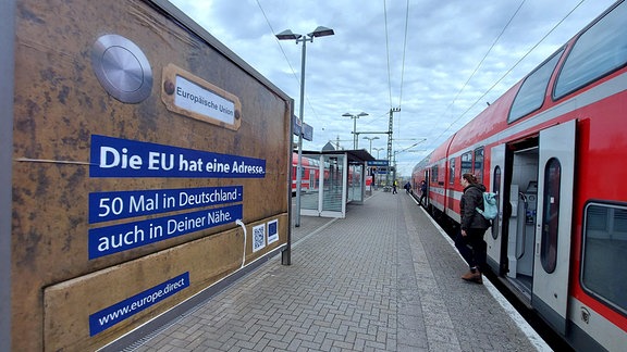 Eine S-Bahn fährt an einen Bahnsteig heran. Gleich öffnen sich die Türen. Am Bahnsteig steht ein riesiges Plakat, auf dem die Europäische Union für sich und eine Homepage-Agebot wirbt.