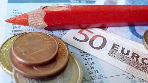 ein Rotstift liegt auf einem Zettel mit Dax-Werten und Geld