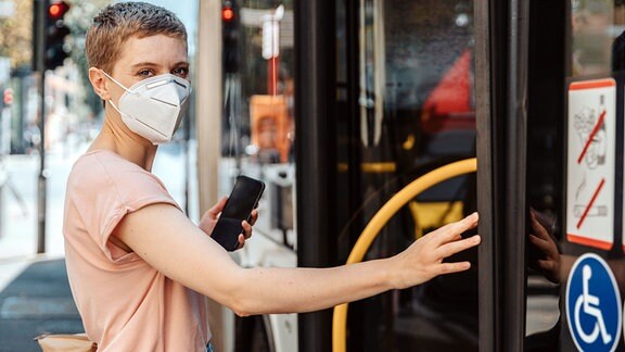Frau mit Atemschutzmaske steig in einen Linienbus.