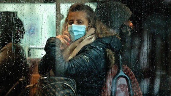Eine Frau mit Mund- und Nasenbedeckung in einem Bus mit regennassen Scheiben