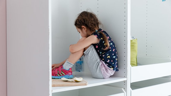 Ein 6-jaehriges Mädchen sitzt in einem ausgeraeumten Schrank (gestellte Szene)