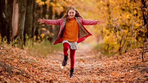 Ein Mädchen läuft mit ausgebreiteten Armen durch eine Herbstlandschaft.