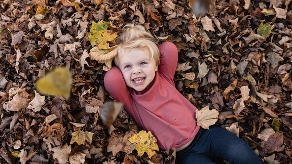 Ein lachendes Kind liegt in einem Laubhaufen.
