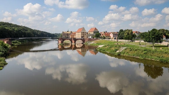 Die Pöppelmannbrücke über der Mulde, die Altstadt von Grimma und die darüber ziehenden Wolken spiegeln sich in dem Fluss.