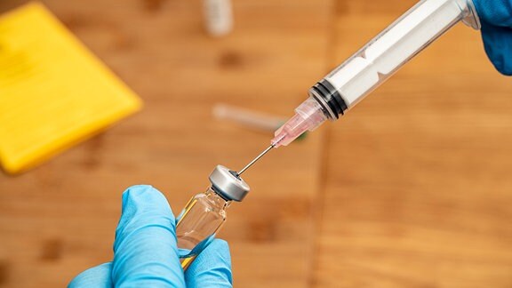 Arzt zieht eine Spritze aus einer Ampulle mit einem Covid 19 Impfstoff für die Impfung in einem Impfzentrum auf, Impfpass des Patienten liegt bereit 