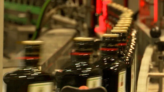 Flaschen in dunkelgrün sind auf einem LAufband der Herstellung zu sehen.