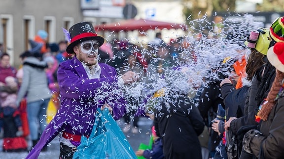 Ein kostümierter Mann Karnevalsteilnehmer wirft Konfetti in die Menschenmenge