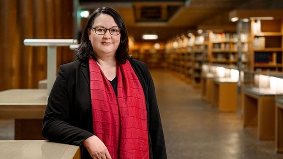 Eine Frau in schwarzem Oberteil und rotem Schal steht in einer Bibliothek