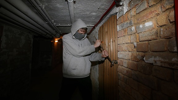 Symbolbild Kellereinbruch, ein Mann bricht einen Keller auf