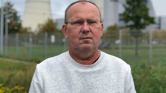 Steffen Sasse steht vor dem Braunkohlekraftwerk "Schwarze Pumpe". Er trägt einen weißen Pullover und eine Brille. 