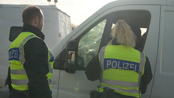 Zwei Polizisten kontrollieren ein Fahrzeug