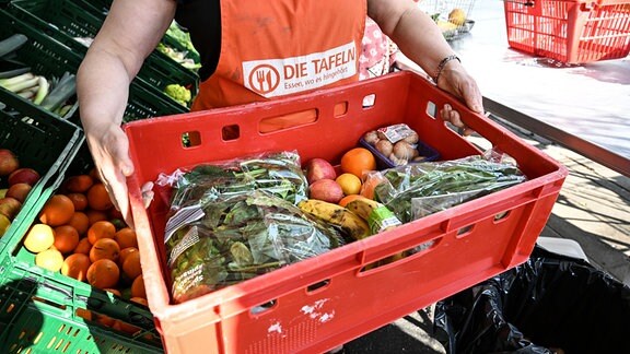 Eine Mitarbeiterin bei den Tafeln trägt eine Kiste voll mit Obst und Gemüse.