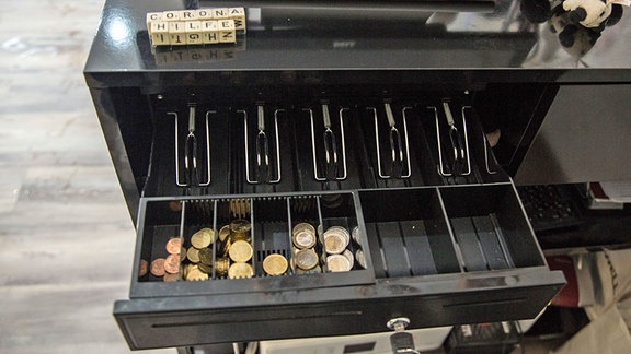 In der offenen Schublade einer Kasse liegt etwas Kleingeld, die Fächer für die Geldscheine sind leer. 