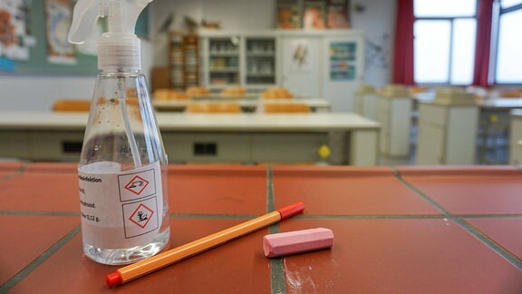 In einem Chemie- Klassenraum einer Schule liegt ein Stueck Kreide, ein Stift und eine Sprühflasche, die mit Desinfektionsmittel gefuellt ist, auf einem Tisch. 