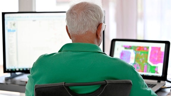 Blick über die Schulter eines älteren Mannes vor zwei Bildschirmen.
