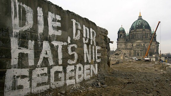 Eine Mauer der Brücke Rathausstraße in Berlin, auf der in weißer Farbe geschrieben steht "Die DDR hat´s nie gegeben", im Hintergrund der Berliner Dom