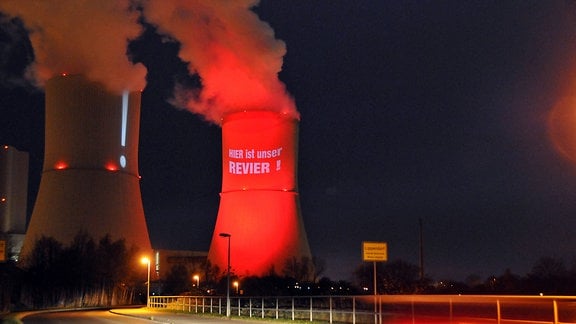 Ein Turm des Kraftwerks Lippendorf wird mit rotem Licht angestrahlt. Darauf steht "Hier ist unser Revier"