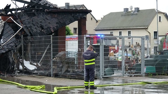 Ein Polizeibeamter steht vor einem abgebrannten Gebäude.