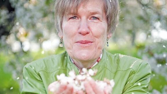 Carmen Goglin pustet in ihre Hände, die voller Kirschblüten sind.