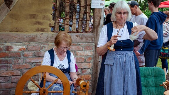 Zwei Frauen arbeiten an einer Dreh- und einer Handspindel.