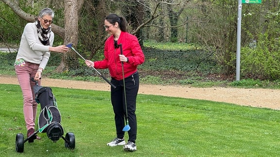 Zwei Frauen tauschen einen Golfschläger.